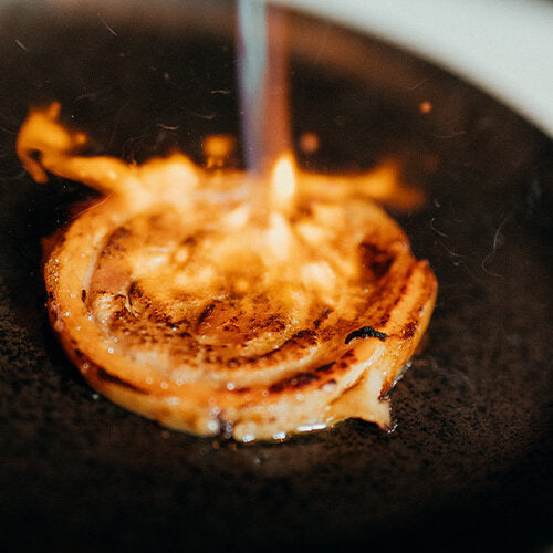 Nahaufnahme von angebratenem Schweinefleisch, das gerade noch flambiert wird